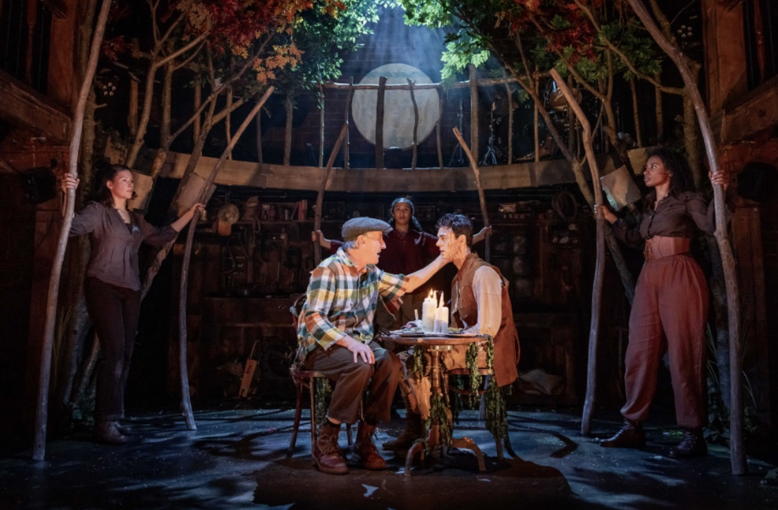 Geppetto and Pinocchio sat at a table surrounded by the company holding tree branches giving the elusion of the inside of a whale stomach