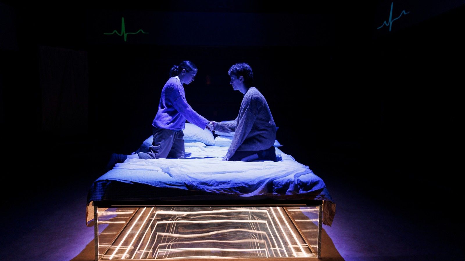 Two people kneel on a bed. Underneath the bed is the illusion of a bottomless pit